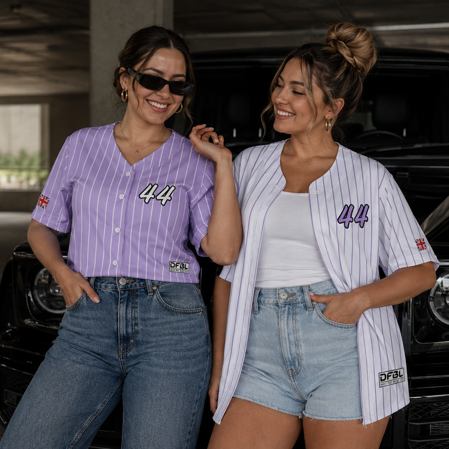 Two women posing in front of a black vehicle inside an underpass. The woman on the left wears a lavender and white pinstripe baseball-style shirt with '44' on the front, paired with blue jeans.